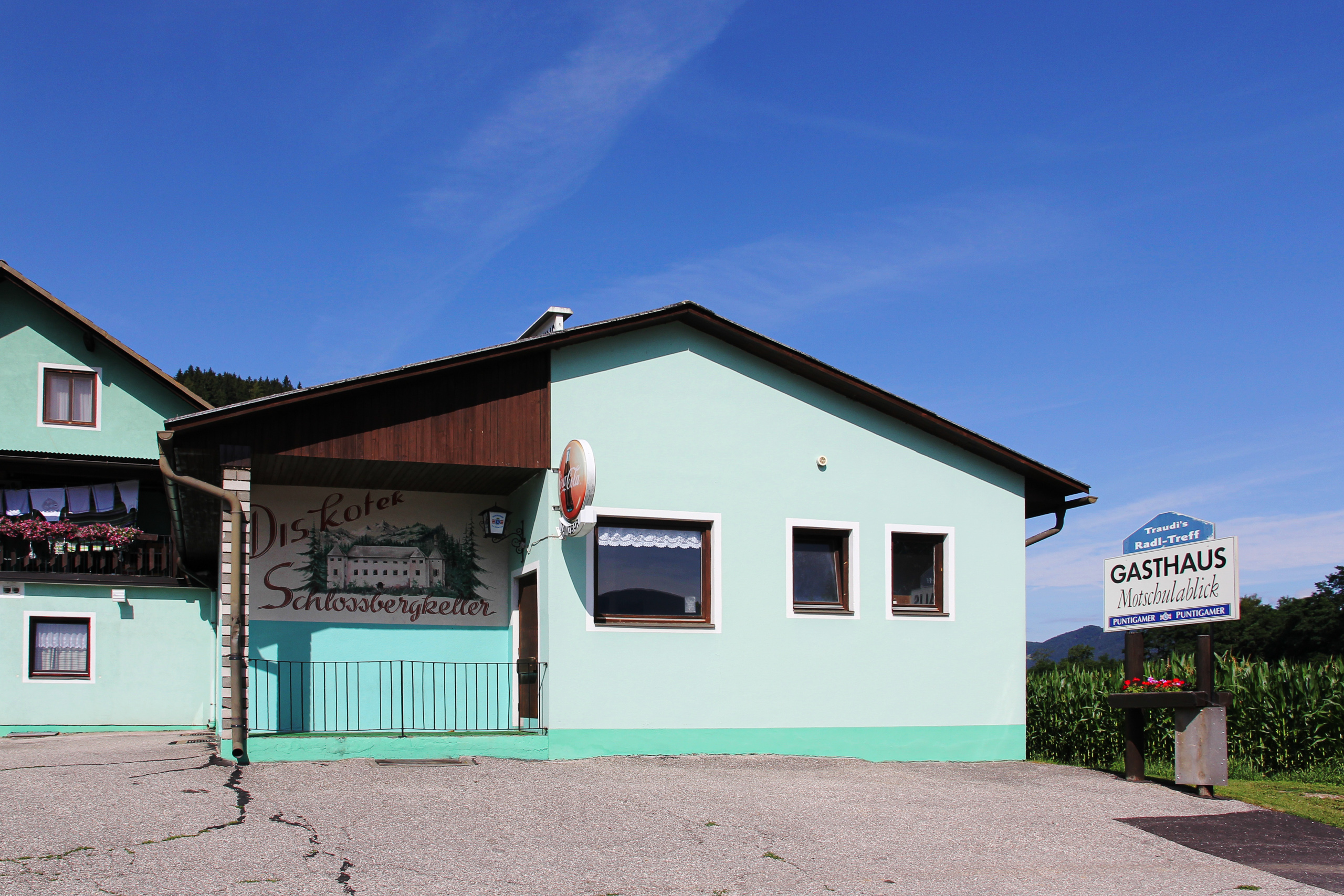 Mintgrünes Gasthaus am Weg, an der Wand die verblasste Reklame des Schlossbergkellers